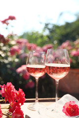 Wall Mural - Glasses of rose wine on table in blooming garden