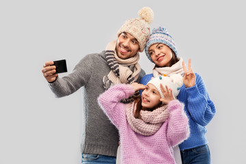 Sticker - family, christmas and technology concept - happy mother, father and little daughter in winter clothes taking selfie by smartphone over grey background