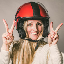 Portrait Of Middle Years Beautiful Blonde, Woman Hero, In Motorcycle Helmet  Gesturing Two V-signs, Peace Symbols, Isolated On Grey Background Looking At Camera.