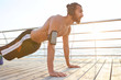 © timtimphoto - Portrait of young bearded sporty gay doing pushups, listening favorite songs on headphones, keeps the plank, doing morning exercises by the sea, warm-up after run, leads healthy active lifestyle.