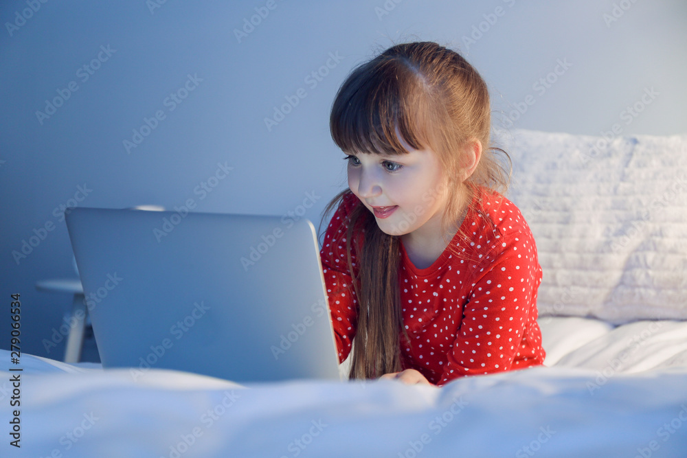 Cute little girl using laptop in bed at night