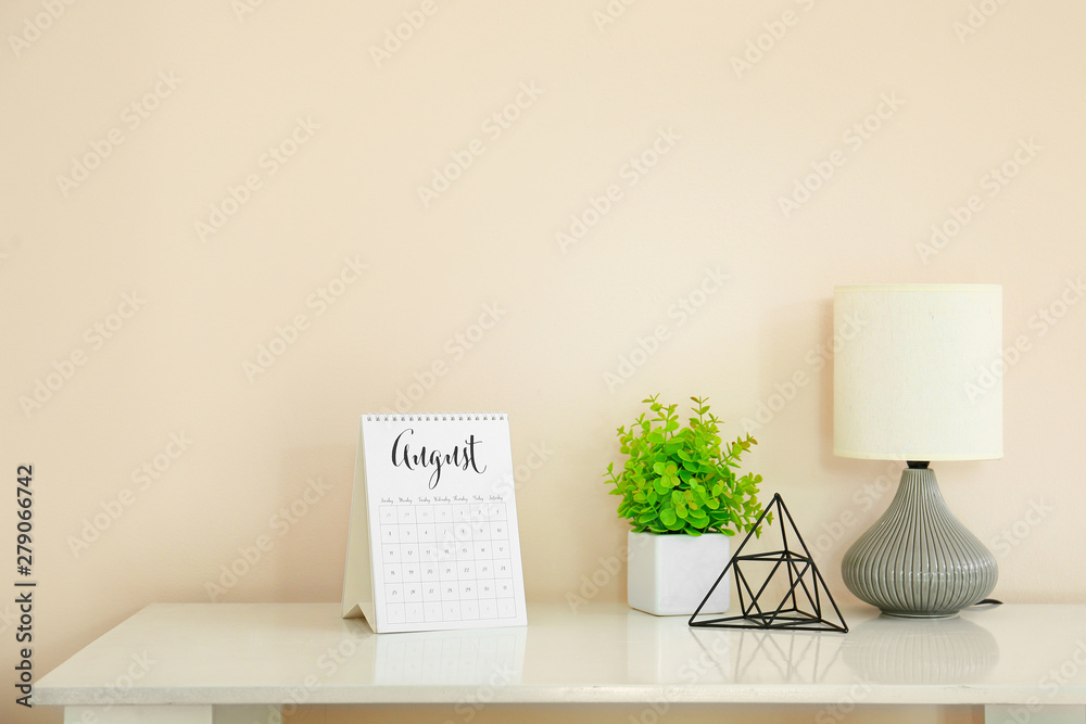 Calendar with lamp and decor on table near light wall in room