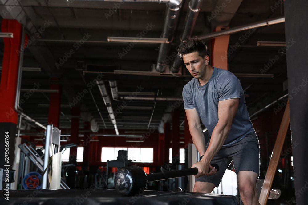 Sporty young man training with tire in gym