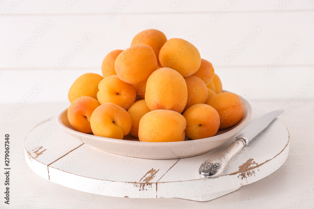 Plate with tasty ripe apricots on white wooden table