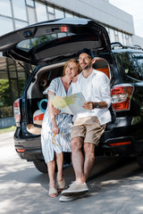 Wall Mural - cheerful man standing near car and beautiful woman while holding map