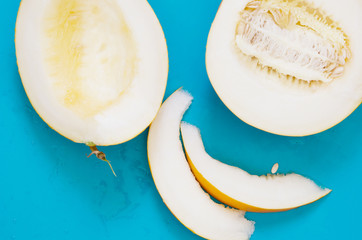 Yellow honeydew melon half with seeds and slices on blue background. - Image