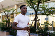 © twinsterphoto - Portrait of Young African American man holding a bottle of water and looking forward in the city street. Male handsome sports person doing workout outdoor in the summer