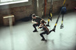 © Friends Stock - Deep squat. Young active couple in sportswear training legs with Trx fitness straps at gym.