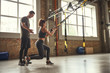 © Friends Stock - Postive workout. Beautiful young woman in sportswear doing trx exercises at gym while her personal trainer is standing next to her