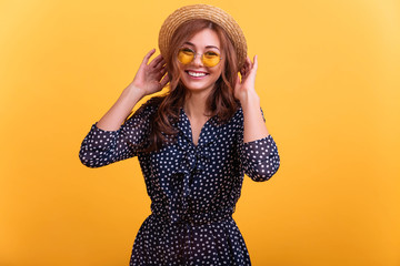 Pretty lady enjoy warm spring breeze making curly hairstyle flight wear polka dot blue dress and straw hat isolated yellow background