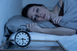Attractive woman in bed staring at alarm clock trying to sleep feeling stressed and sleepless