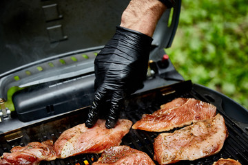 Wall Mural - Grilled turkey meat. Hand of young man grilling some meat meat skewers on huge gas grill