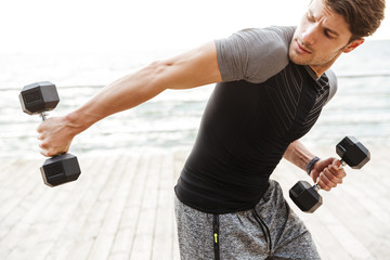 Wall Mural - Strong handsome concentrated young sports man outdoors at beach make exercises for triceps arms with dumbbells.