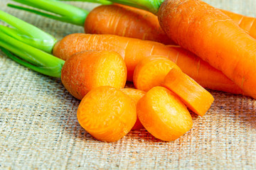 Wall Mural - Fresh sliced carrots with green petiole on a jute background. Raw carrots full of vitamins ready for processing