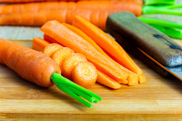 Wall Mural - Fresh sliced carrots with green petiole on a wooden cutting board with knife. Raw carrots full of vitamins ready for processing