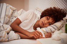 Millennial African American Woman Lying Ill In Bed Looking To Camera, Close Up