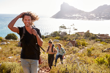 young adult white man hiking with friends in countryside by the coast smiling to camera