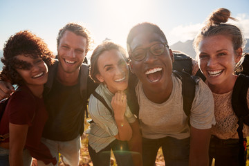 young adult friends on a hike celebrate reaching the summit, smiling to camera, close up