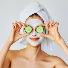 Wall Mural - beautiful young woman with facial mask on her face holding slices of cucumber. skin care and treatme