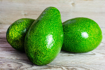 Wall Mural - Three whole fruits of green avocado on wooden background. A juicy green avocado on a wooden kitchen table. Healthy tropical fruits.