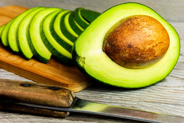 Wall Mural - Slices of green avocado on a wooden cutting board. A juicy green avocado on a wooden kitchen table. Healthy tropical fruits.