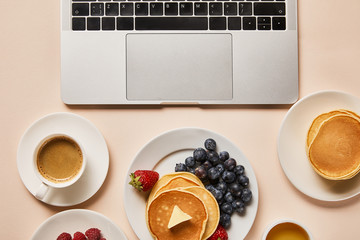 Poster - top view of tasty breakfast with pancakes, berries, cup of coffee and honey near laptop