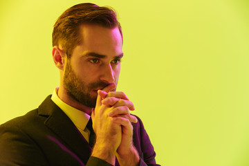 Image of focused young businessman in formal suit holding hands at his mouth