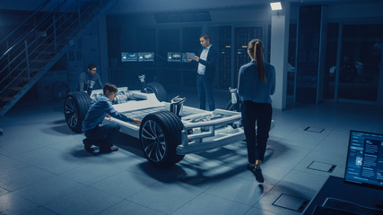 Fototapete - Team of Automotive Engineers Working on Electric Car Platform Chassis, Taking Measures, working with 3D CAD Software, Analysing Efficiency. Vehicle Frame with Wheels, Engine and Battery.