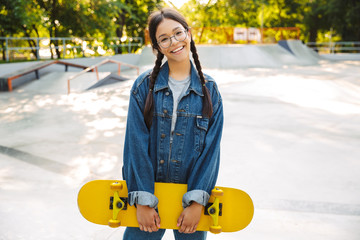 Poster - Image of joyful girl smiling and rejoicing while holding skateboard in skate park