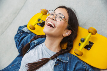 Poster - Image of happy girl laughing and rejoicing while holding skateboard over concrete wall