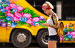 © Artem Markin - A blonde woman with a phone in hand is standing against the background of a yellow bus. Modern girl wears a red bandage, arms tattooed.