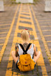 © Artem Markin - Modern girl sits with his back to the camera on a road marking. Carries a yellow backpack, arms tattooed