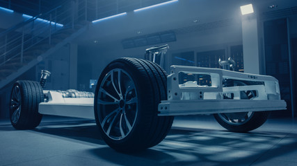 Concept of Authentic Electric Car Platform Chassis Prototype Standing in Industrial Machinery Design Laboratory. Hybrid Axel Frame include Wheels, Suspension, Engine, Brakes and Battery. 