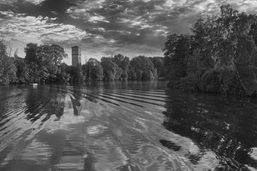 Wall Mural - River with reflections from clouds and a tower and forest on the left side and forest and sun on the right side