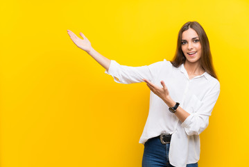 Wall Mural - Young woman over isolated yellow background extending hands to the side for inviting to come