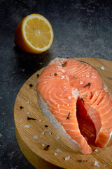 Salmon steak with lemon, fish fillet, large cut portions on a cutting Board on a dark table. Vertical.