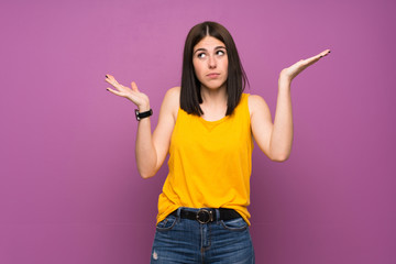 Young woman over isolated purple wall making doubts gesture