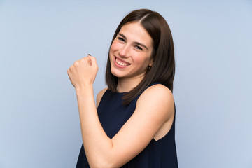 Young woman over isolated blue wall celebrating a victory