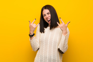 Wall Mural - Young woman over isolated yellow wall making rock gesture