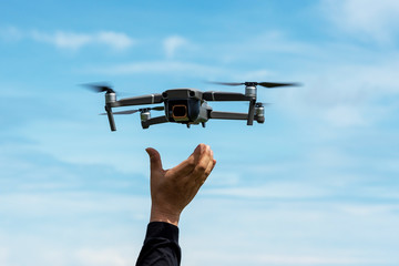 hands reaching for drone against blue sky