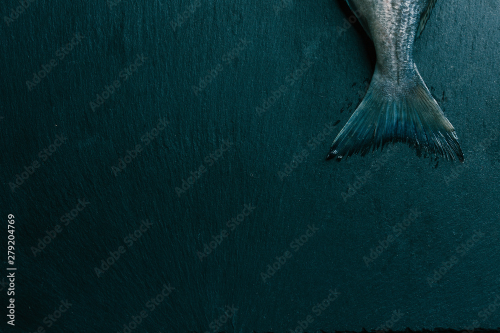Isolated photo of raw fish tail on black slate surface - obrazy, fototapety, plakaty 