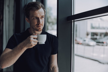 Wall Mural - Handsome man with cup standing near the window