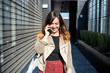© Cavan Images - Woman smiling and talking on phone while walking in city