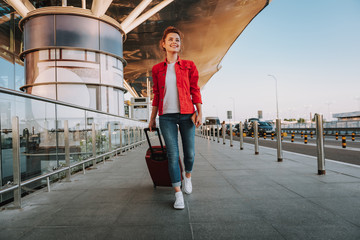 Charming young woman with travel suitcase walking on the street