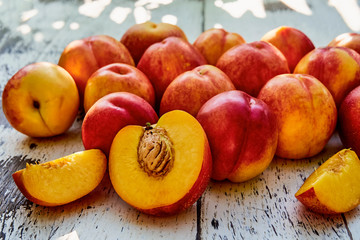 Ripe peaches with leaves on the old wooden table against the background of green leaves. Fresh sweet sliced peaches in the garden. Soft selective focus