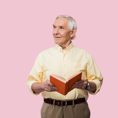 Wall Mural - cheerful retired man holding book and smiling isolated on pink