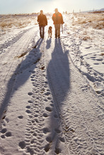 Two Hunters Walking Down Snowy Trail With Dog