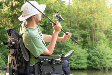 Wall Mural - Happy man in a electric wheelchair throwing fishing pole at the beautiful pond in natue on a sunny day