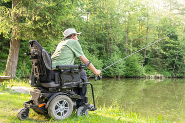 Wall Mural - Happy man in a electric wheelchair throwing fishing pole at the beautiful pond in natue on a sunny day