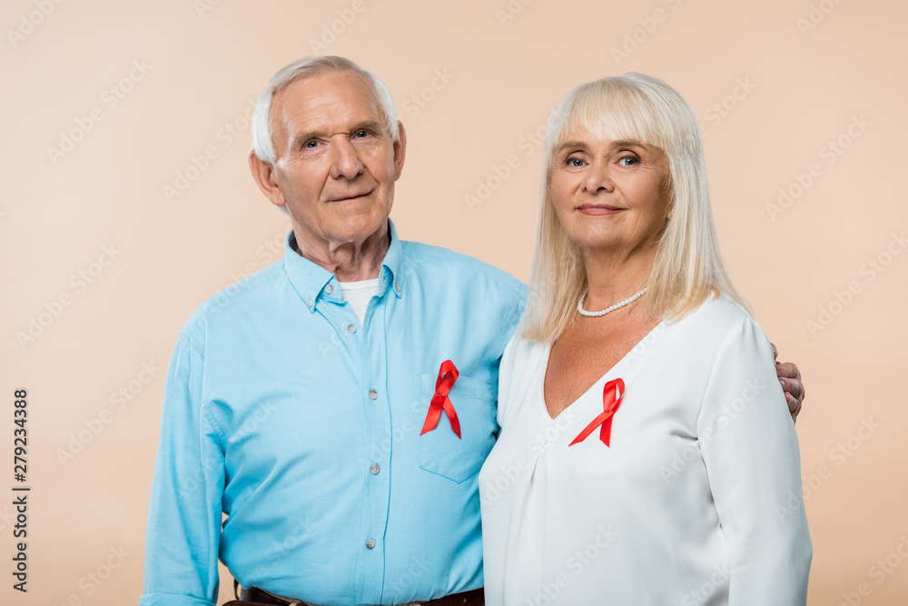 happy senior couple with red ribbons as hiv awareness isolated on beige - obrazy, fototapety, plakaty 